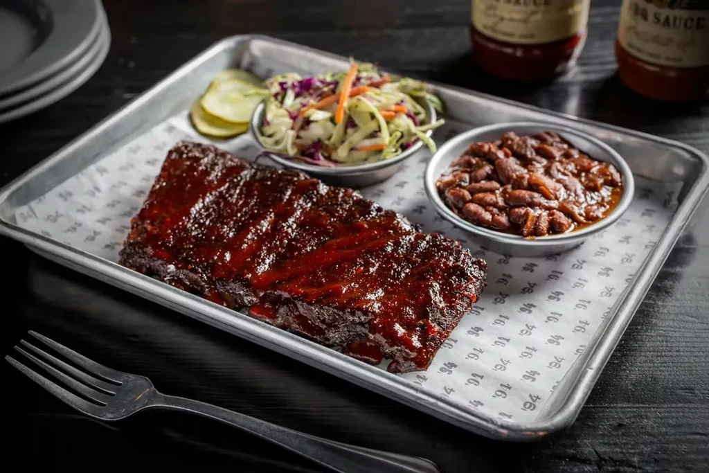 Barbecue ribs on a metal tray with coleslaw and beans.