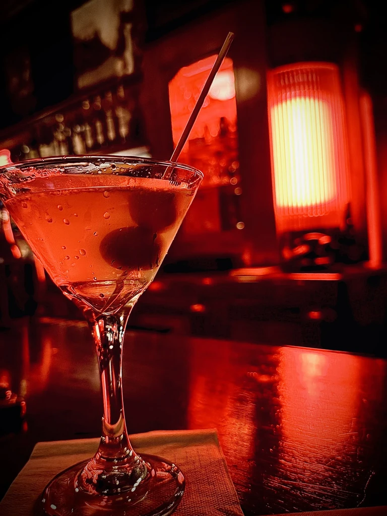 Martini glass with amber cocktail and olives on a bar.