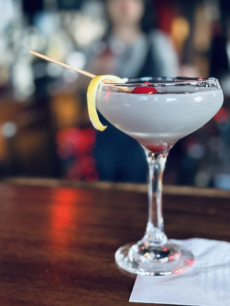 Opaque cocktail in a coupe glass with lemon peel and cherries.