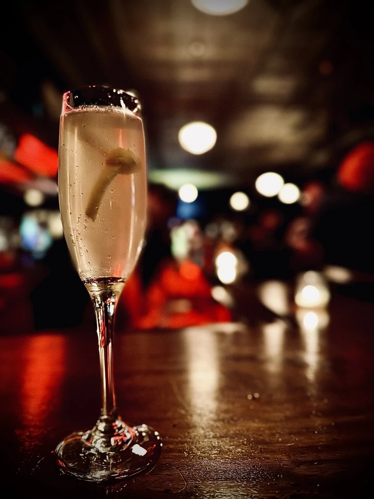Light-colored sparkling drink with a green garnish in a champagne flute.