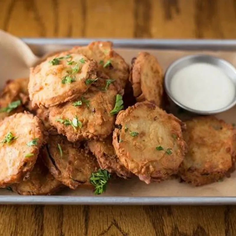 Fried pickles with a white dipping sauce on a metal tray.