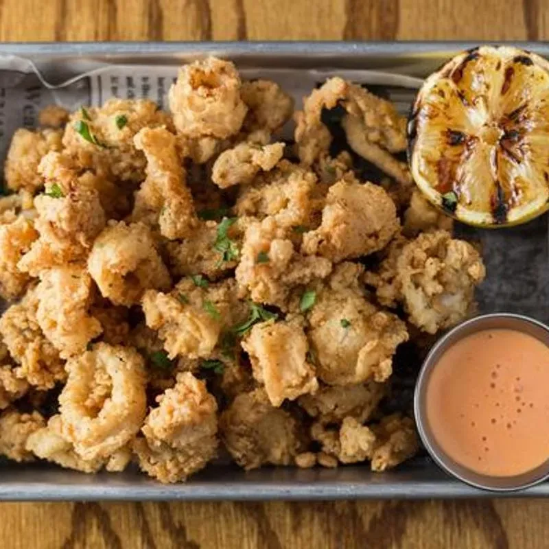 Fried calamari with a grilled lemon and dipping sauce on a metal tray.