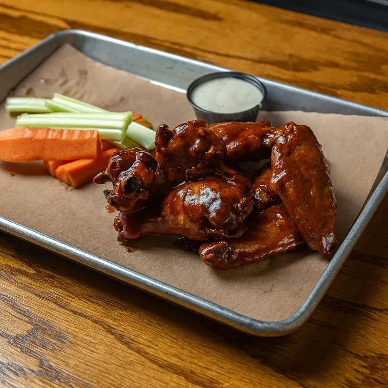 Chicken wings, celery, carrots, and dipping sauce on a metal tray.