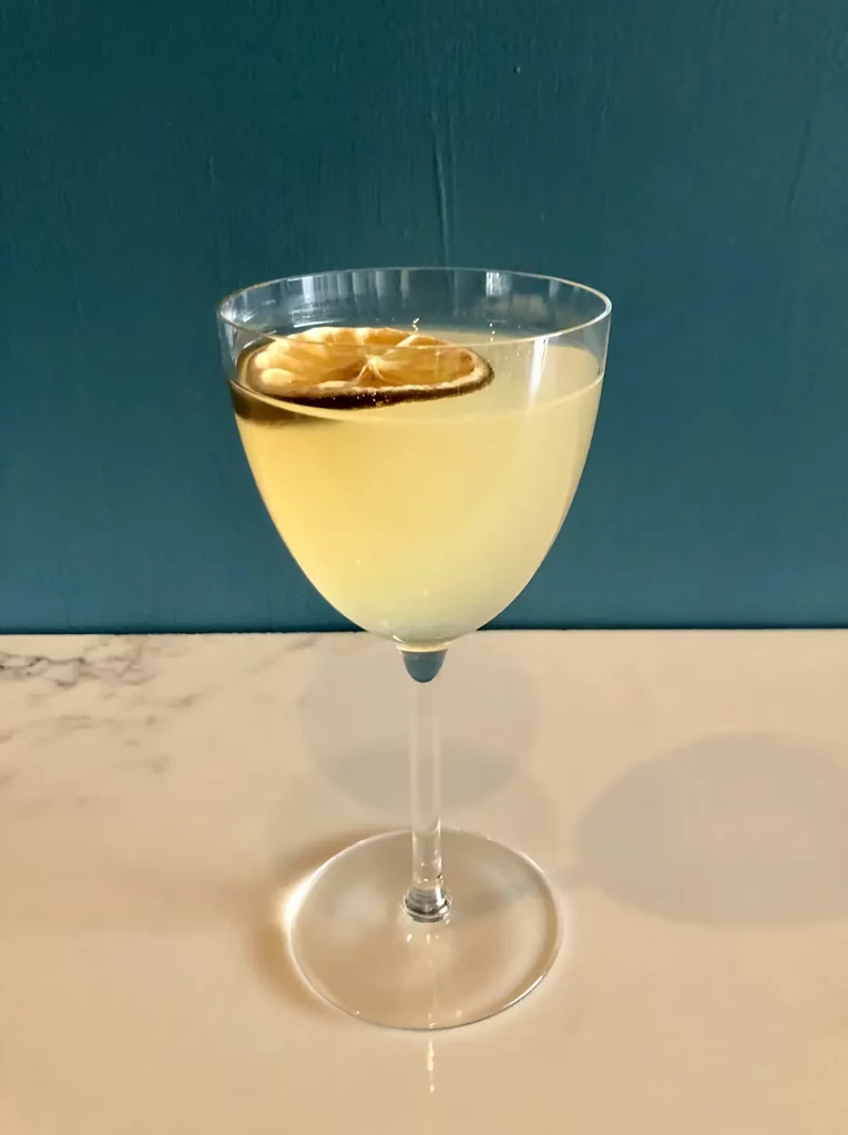 Pale cocktail with dried citrus slice on a light countertop.