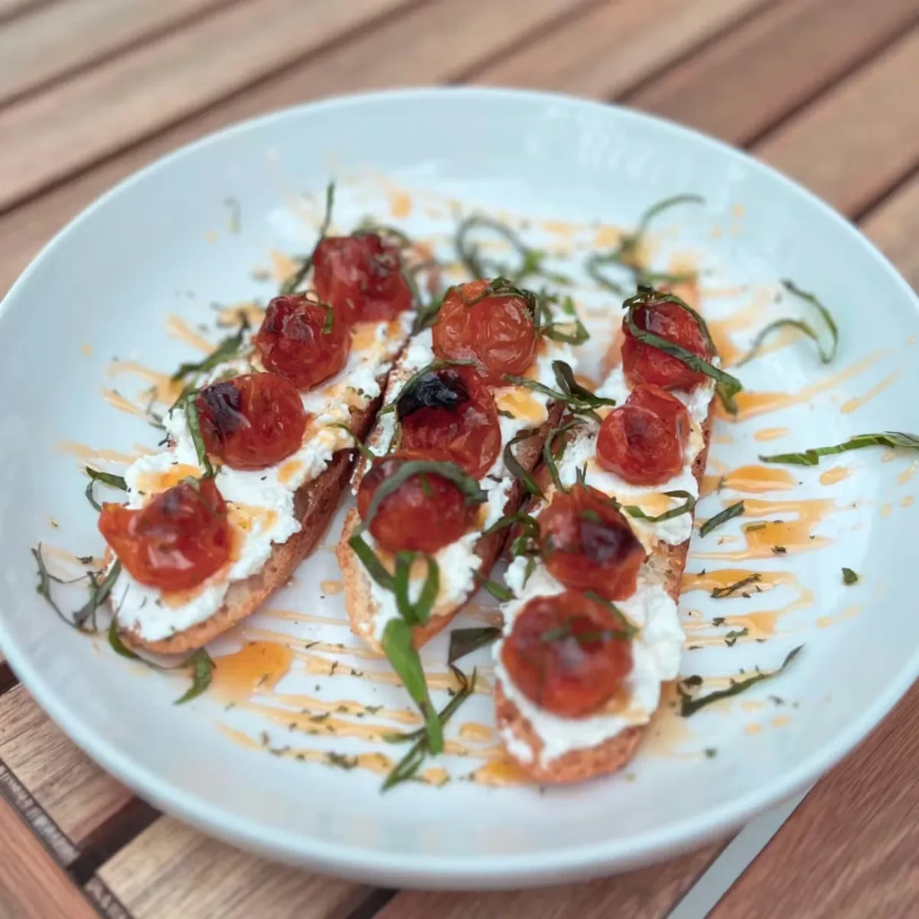 Bruschetta with creamy cheese, roasted tomatoes, and herb garnish.