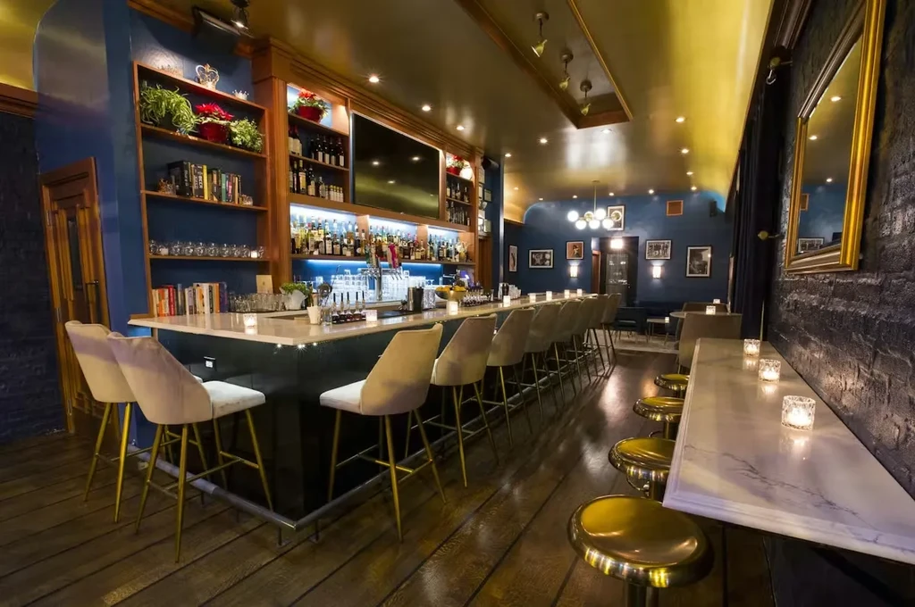 Dimly lit bar with a long counter, stools, and bookshelves.