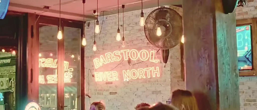 Neon sign "BARSTOOL RIVER NORTH" on a white brick wall.