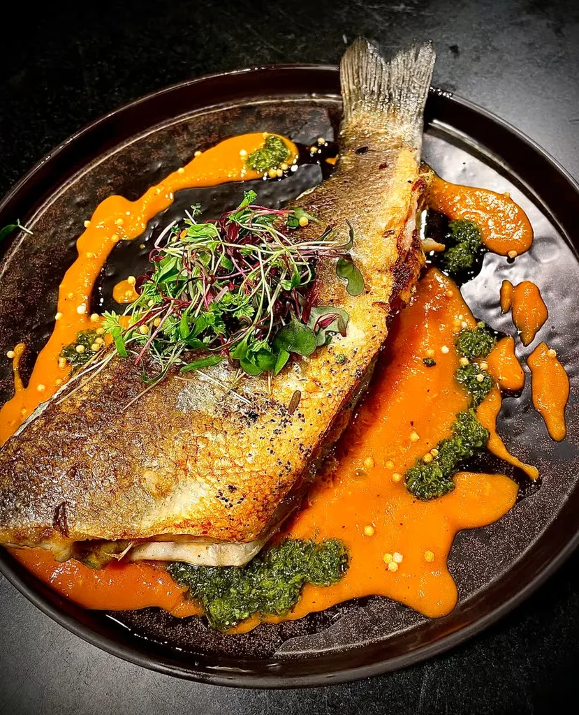 Whole roasted fish garnished with microgreens and two sauces.