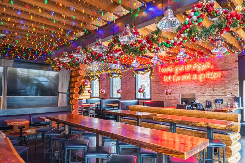Festive restaurant interior with Christmas lights, high-top tables, and log walls.