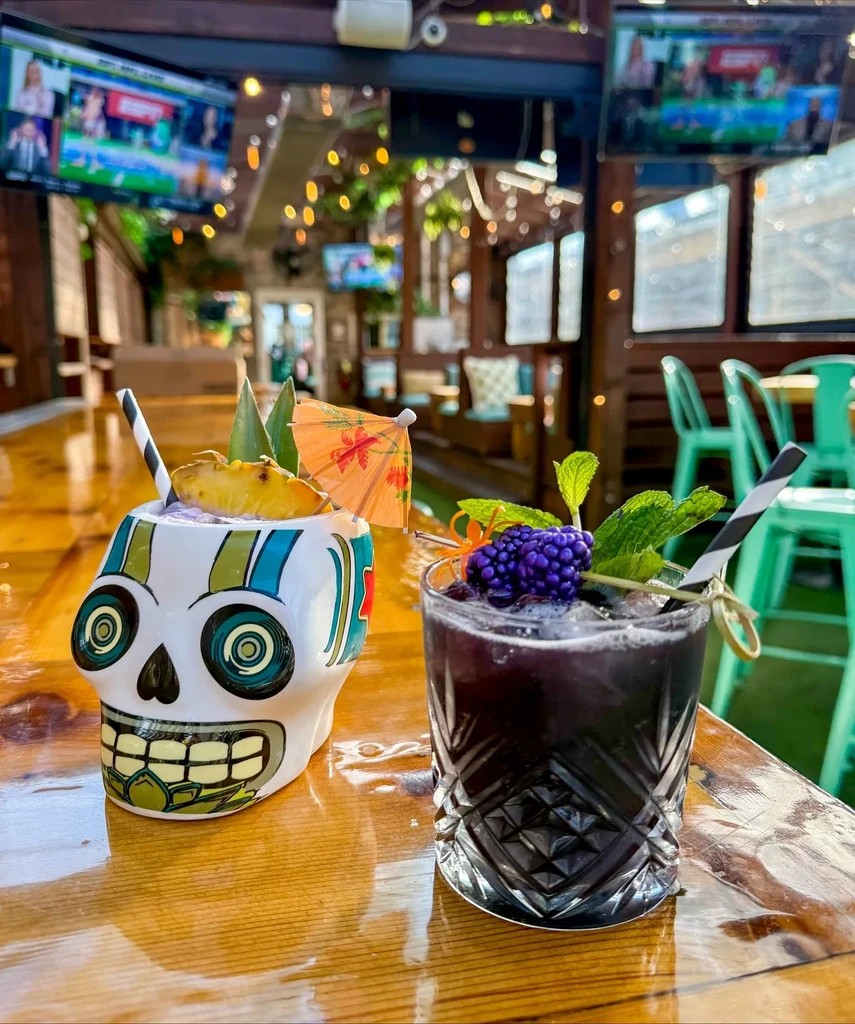 Two garnished cocktails sit on a wooden bar top.