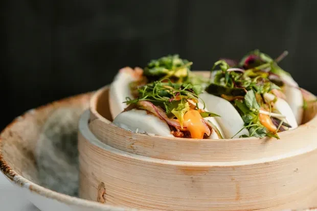 Bao buns with herbs and sauce in a bamboo steamer.