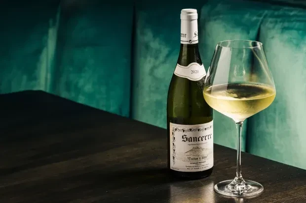 Sancerre white wine bottle and glass on a dark wooden table.