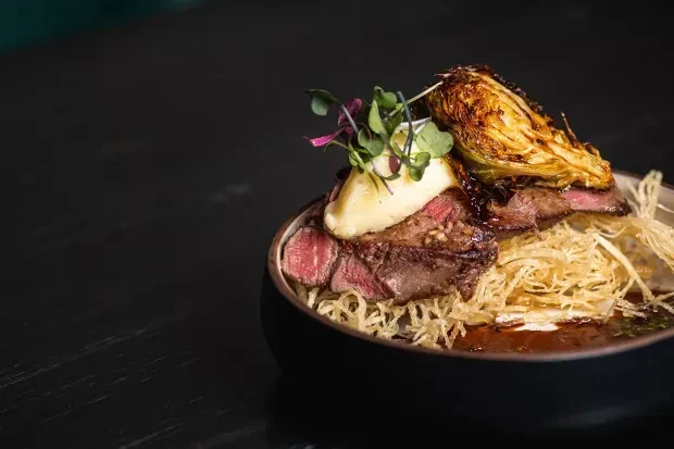 Medium-rare sliced steak with mashed potatoes, microgreens, and a vegetable.