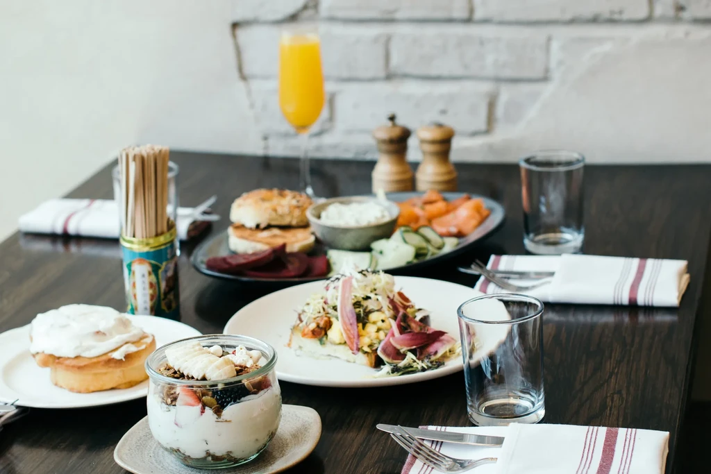 Breakfast spread with yogurt, cinnamon roll, open-faced sandwich, bagels, mimosa.