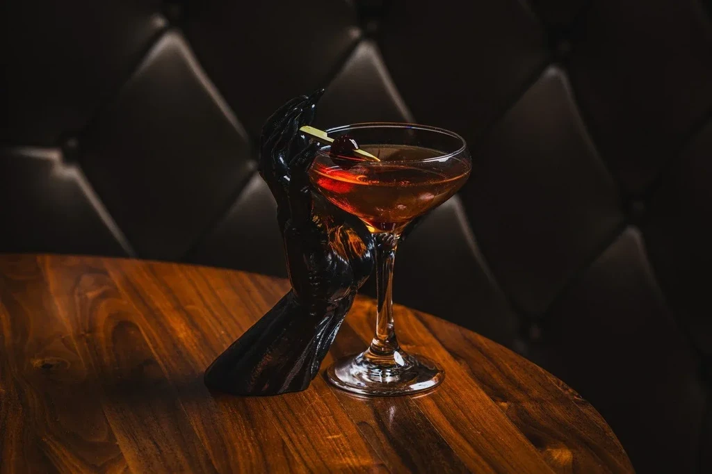 Reddish-brown cocktail in coupe glass held by black hand sculpture.