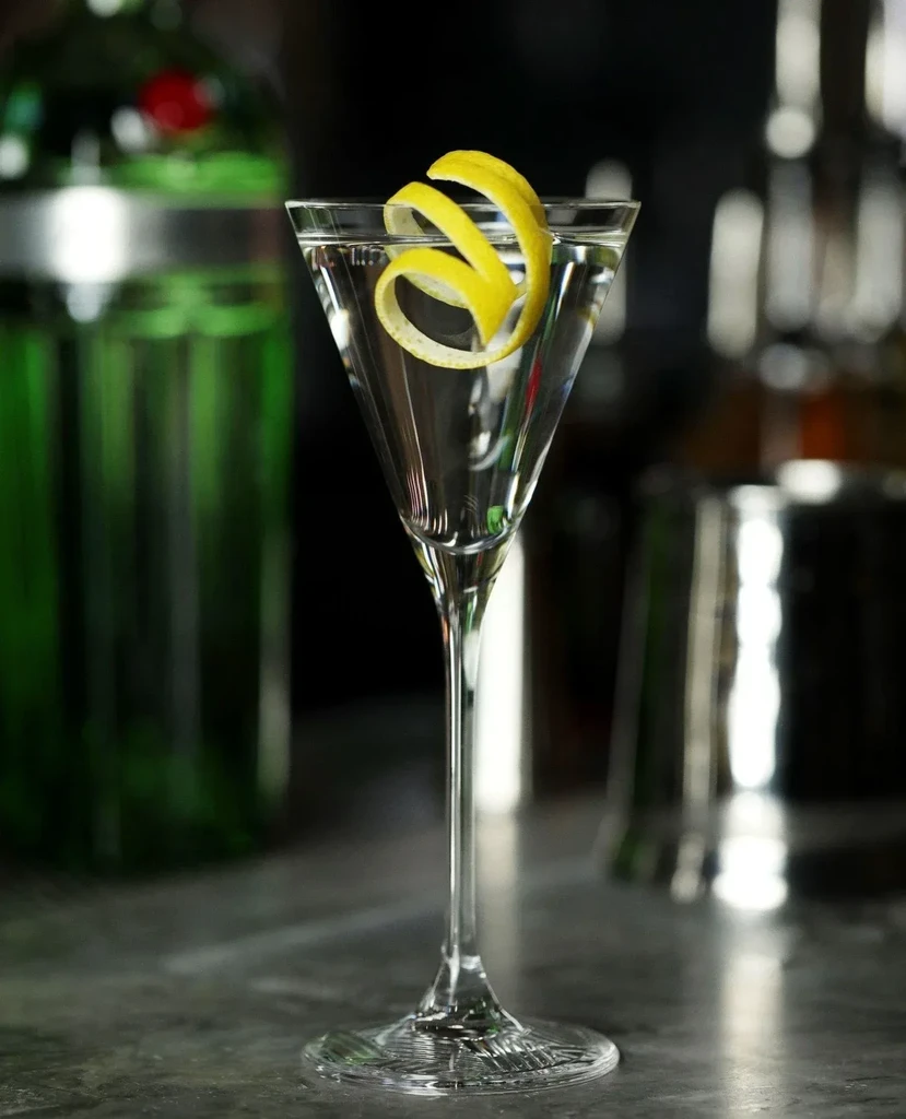 Martini glass with clear liquid and lemon peel on a bar.