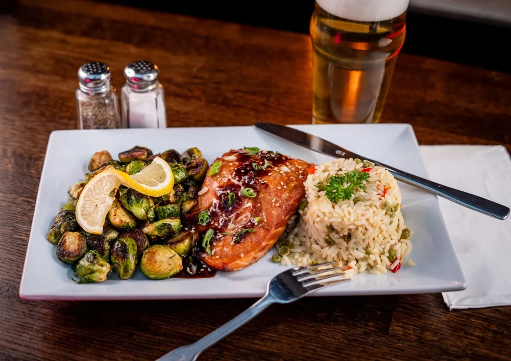 Glazed salmon, rice pilaf, Brussels sprouts, beer on wooden table.