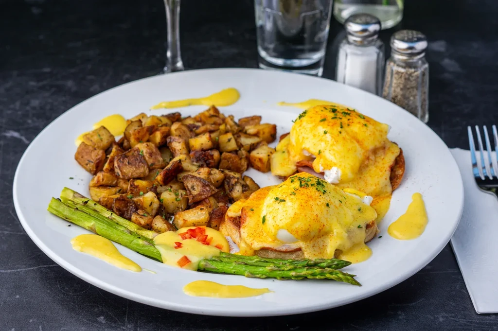Eggs Benedict, roasted potatoes, and asparagus on a white plate.