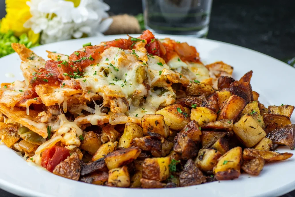 Chilaquiles with melted cheese and roasted potatoes on a white plate.