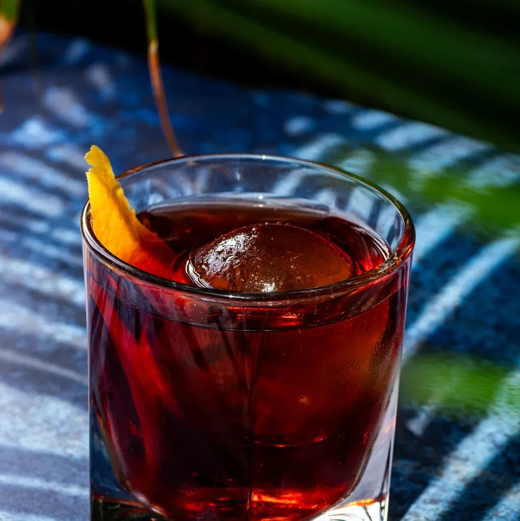 Cocktail with a spherical ice cube and orange peel garnish.