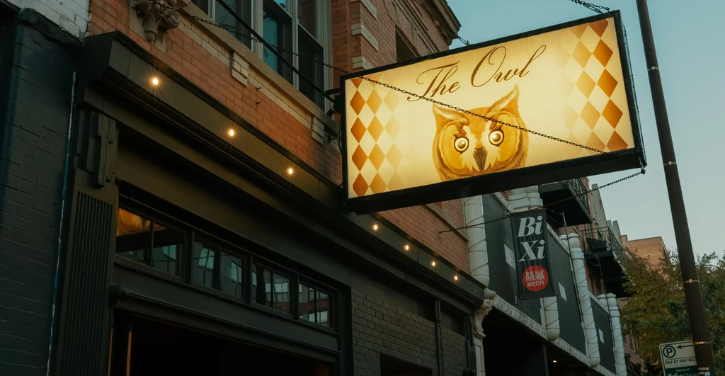 Exterior of The Owl restaurant with an owl sign and string lights.