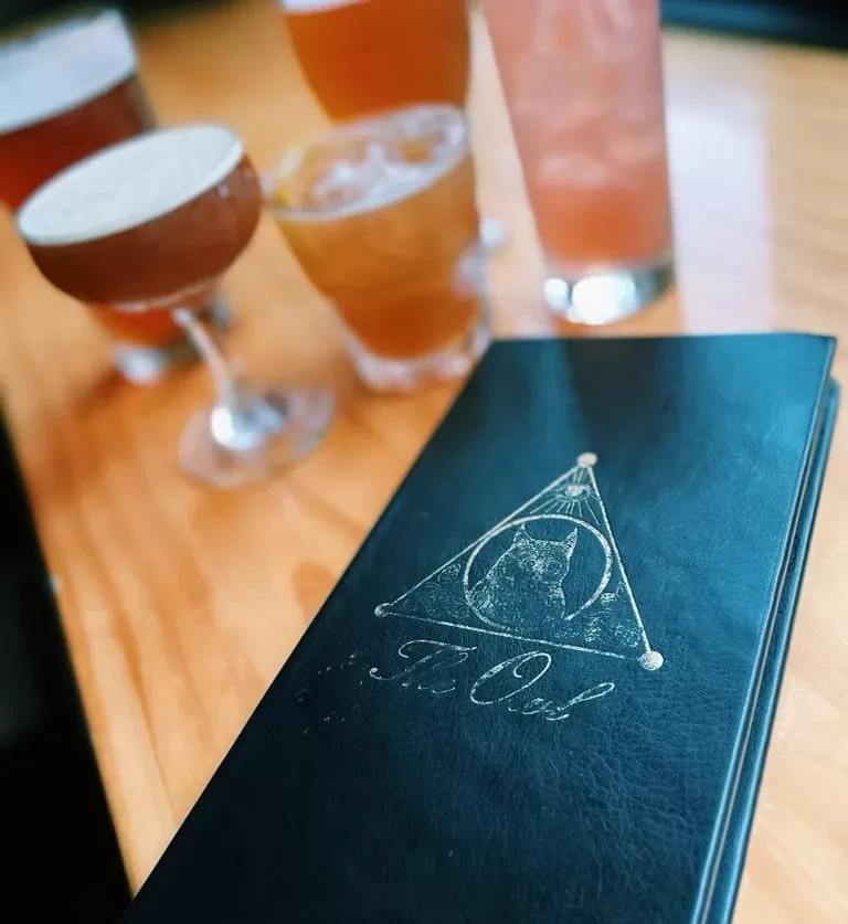 Dark menu with "The Cat" logo on a light wooden table.