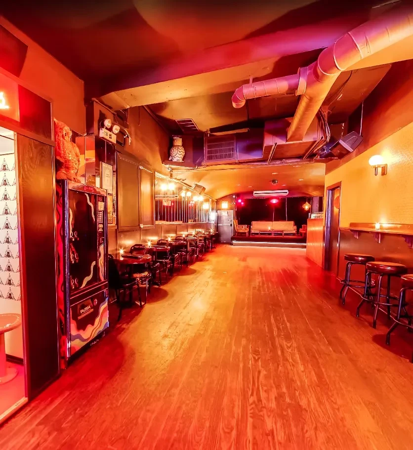 Interior of a bar with red lighting, tables, and a bar area.