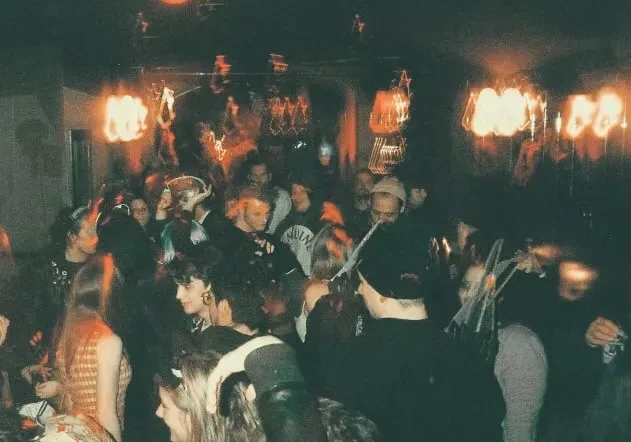 Grainy photo of a crowded, dimly lit indoor social gathering.