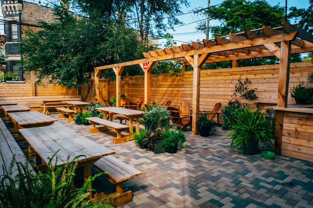 Outdoor patio with wooden picnic tables, brick floor, and plants.