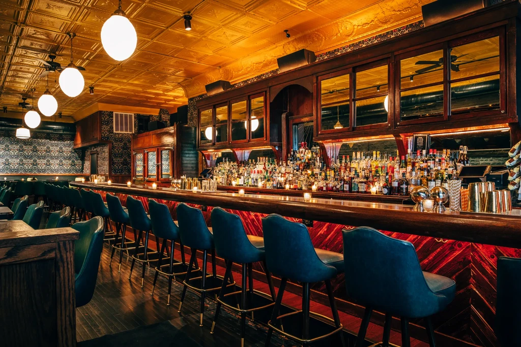 Sophisticated bar interior with long counter, liquor bottles, and bar stools.