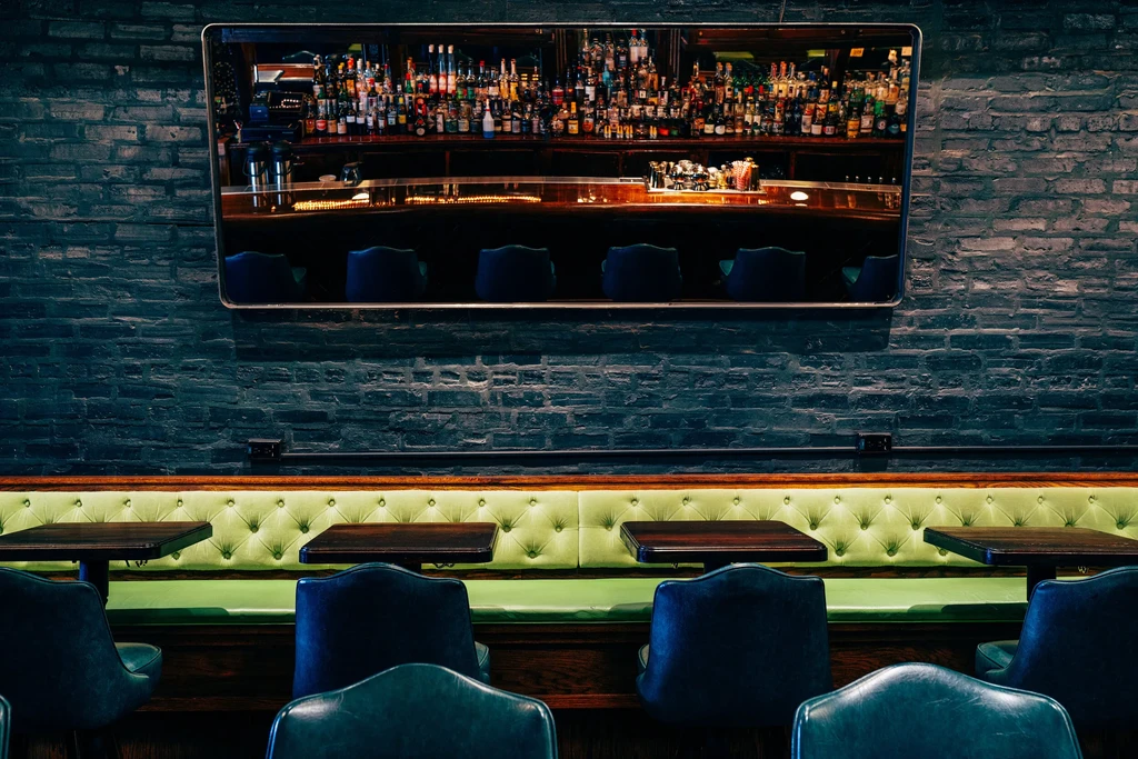 Restaurant interior with lime green booth, tables, and mirror reflecting bar.