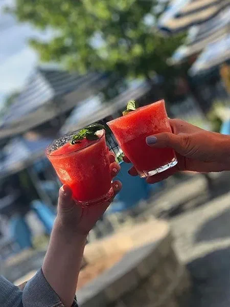 Two hands clinking glasses of red frozen drinks outdoors.