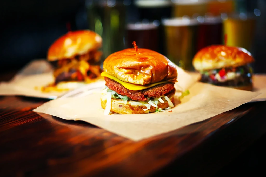 Three gourmet burgers on a wooden table, one in sharp focus.
