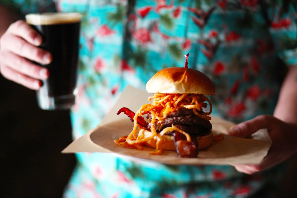 Person holding a large gourmet burger and a glass of beer.