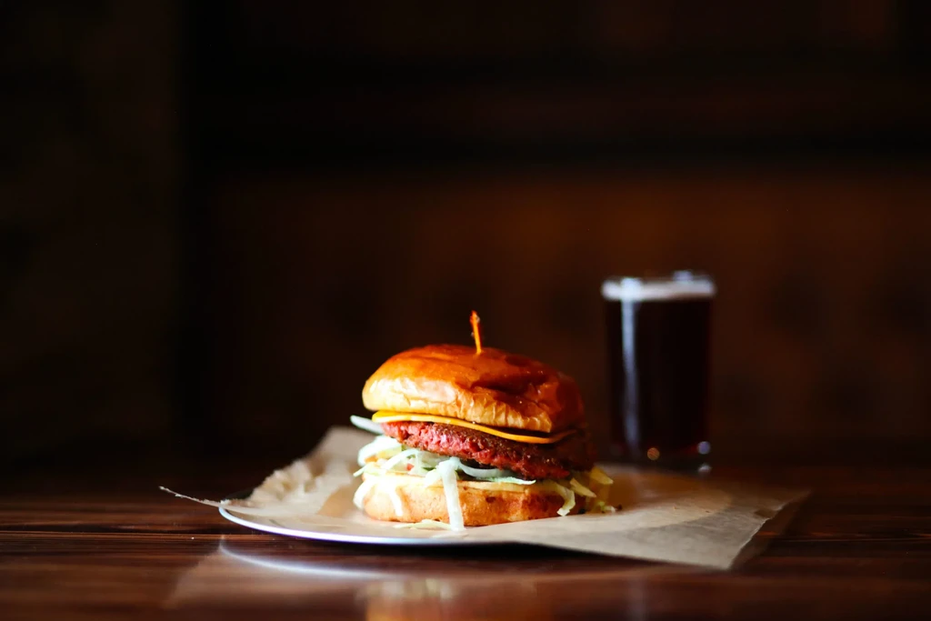 Burger with cheese, lettuce, and a dark beer on a wooden table.