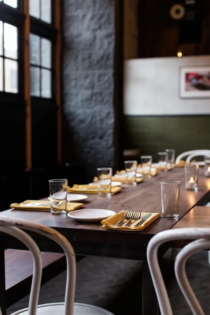 Long dining table set with plates, napkins, and silverware in a restaurant.