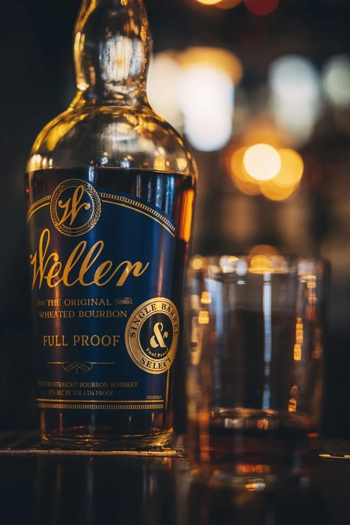 Weller Full Proof bourbon bottle and empty glass on bar.