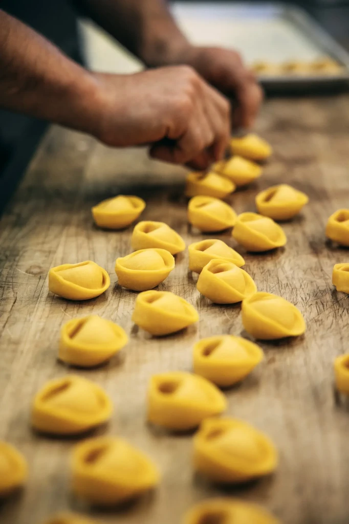 Freshly-made pasta shapes on a wooden surface with hands in background.