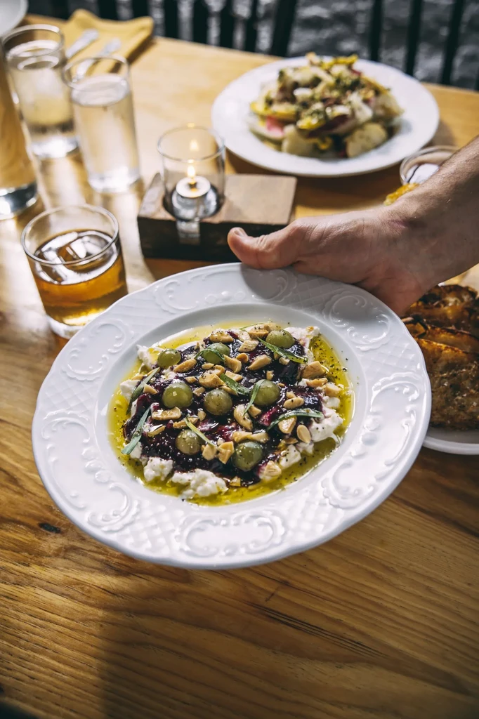 Ornate plate with creamy dish, dark sauce, grapes, nuts, and herbs.