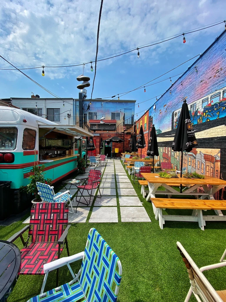 Outdoor restaurant patio with food truck, picnic tables, and colorful chairs.