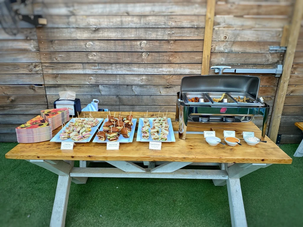Outdoor buffet on picnic table with pizza, appetizers, hot food.