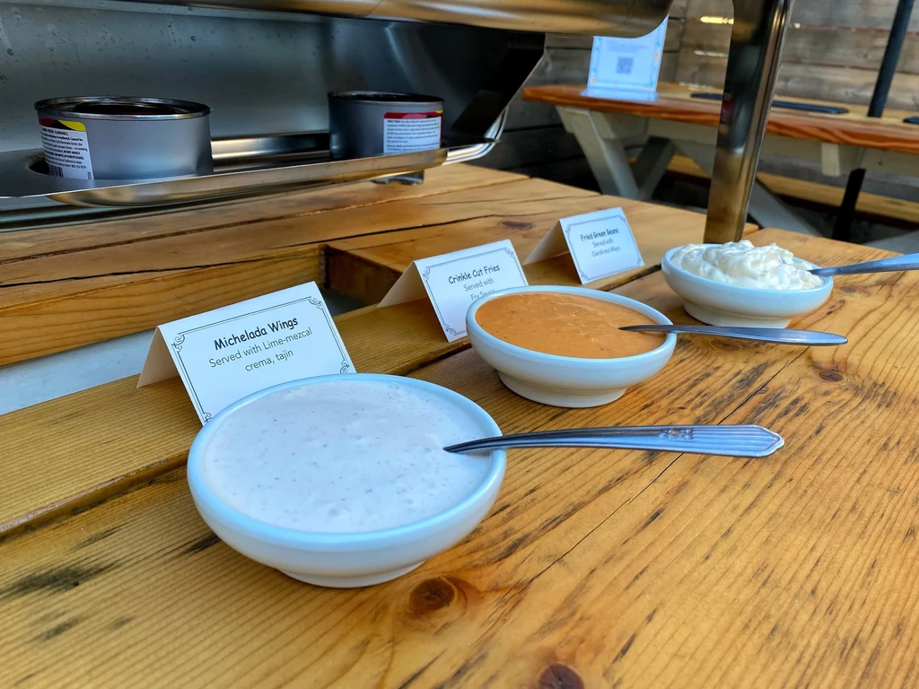Sauces and dips with tent cards on a rustic wooden table.