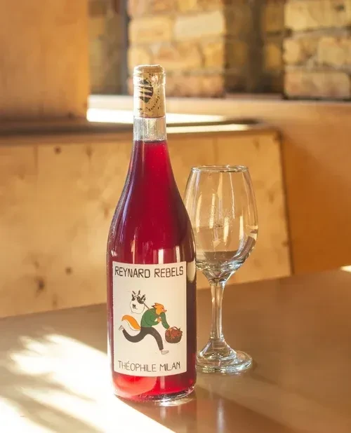 Red wine bottle with glass on wooden table.