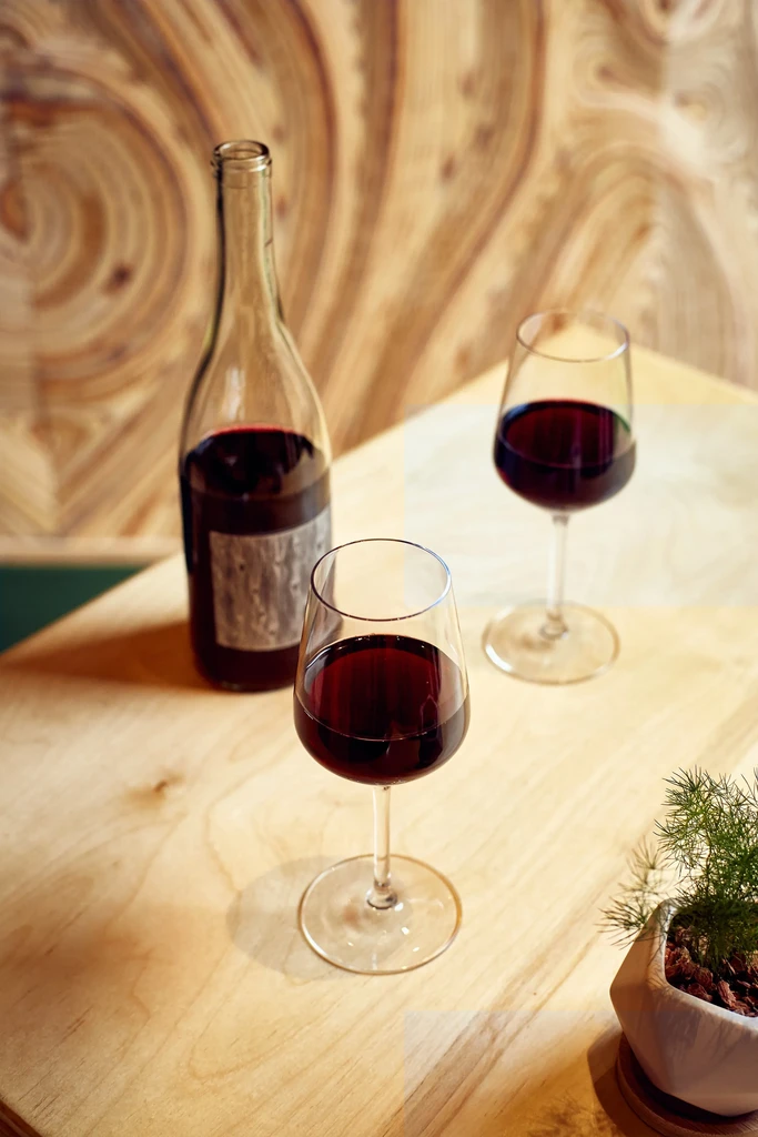 Red wine bottle, two full glasses, and plant on a wooden table.