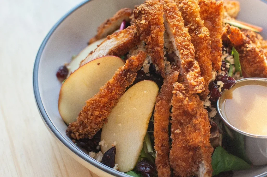 Salad with fried chicken, red apple slices, and cranberries.