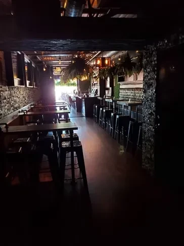 Dimly lit bar interior with high-top tables and a moss wall.