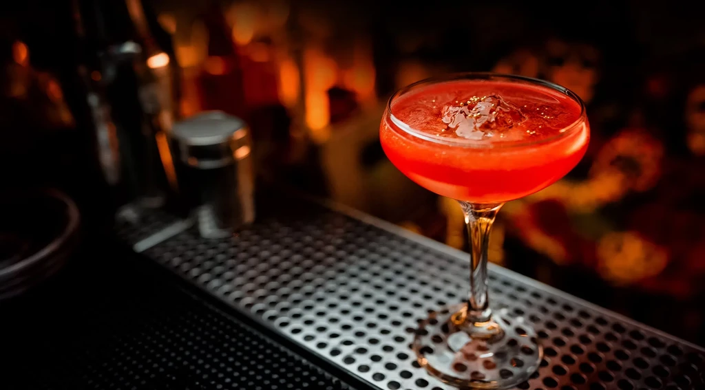 Red frothy cocktail in a coupe glass on a bar mat.