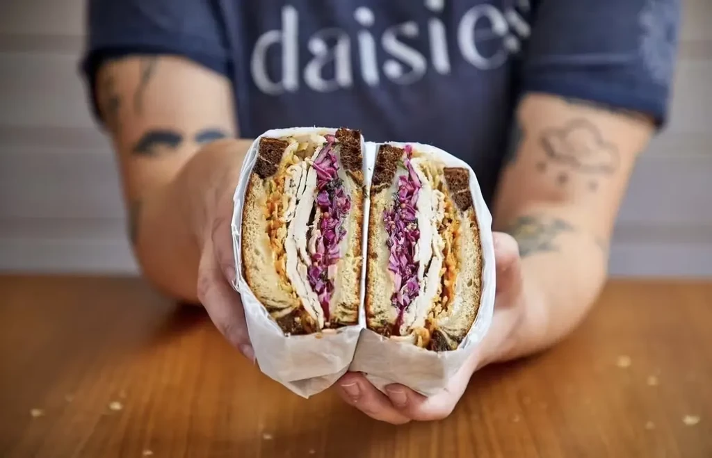 Hands hold a halved sandwich with turkey, sauce, and purple cabbage.