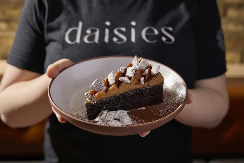 Person holds a dessert slice with frosting, crispy pieces, and cocoa.
