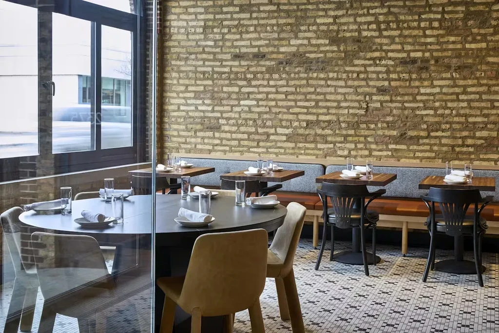 Restaurant interior with set tables, mosaic floor, and exposed brick wall.